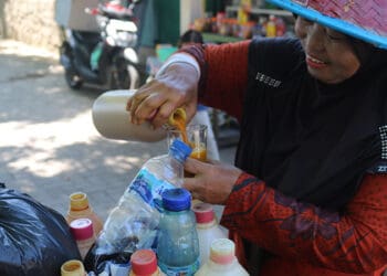 Sartiwi atau yang akrab di sapa Mbak Tini, salah seorang penjual jamu puluhan tahun di Kota Padang sedang menuangkan jamu untuk pelanggannya di kawasan Batang Arau Kota Padang, Kamis, 25 Mei 2023 (Foto:Fitria Marlina)