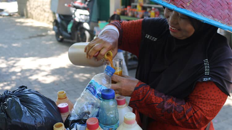 Sartiwi atau yang akrab di sapa Mbak Tini, salah seorang penjual jamu puluhan tahun di Kota Padang sedang menuangkan jamu untuk pelanggannya di kawasan Batang Arau Kota Padang, Kamis, 25 Mei 2023 (Foto:Fitria Marlina)